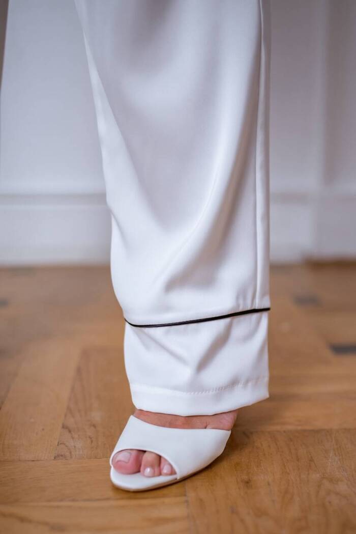 Spodnie Odette - satynowe w kolorze ecru z ozdobnym czarnym pajpingiem u dołu nogawki