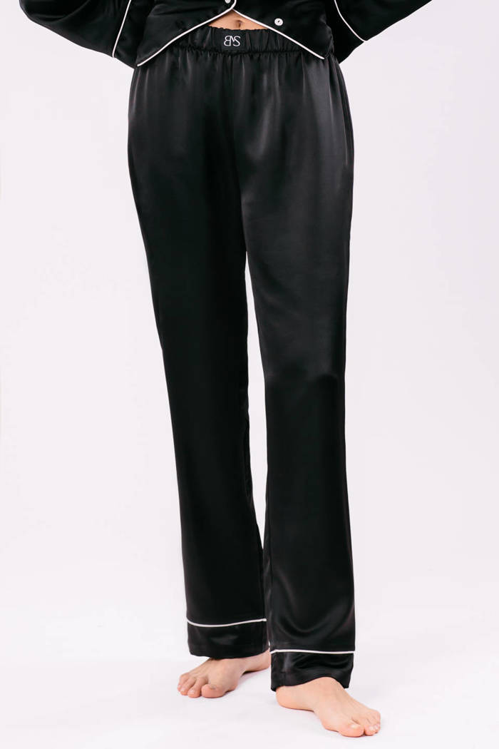 Spodnie Odette - satynowe w kolorze głębokiej czerni z ozdobnym białym pajpingiem u dołu nogawki