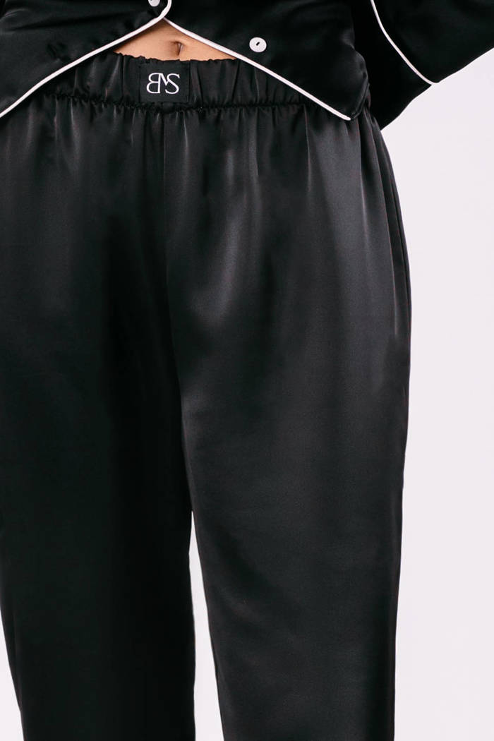 Spodnie Odette - satynowe w kolorze głębokiej czerni z ozdobnym białym pajpingiem u dołu nogawki